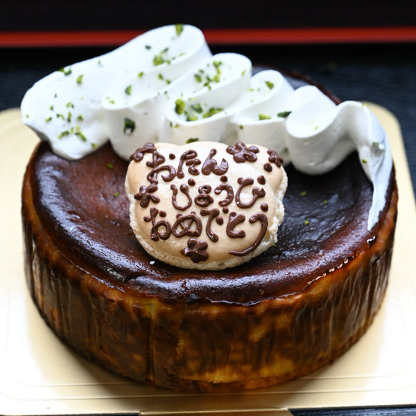 ピスタチオのバスクチーズケーキ(ホール)の写真。生クリームと刻みピスタチオ、マカロンのメッセージプレート付き写真