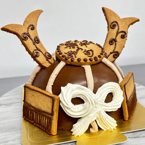 生チョコでコーティングしたドーム型のチョコレートケーキに、生クリームのリボン、端午の節句とかかれたクッキー、クッキーでできたツノなどの細工をデコレーションした、こどもの日(端午の節句)用の立体かぶとケーキの写真。
