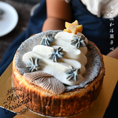 クリスマス仕様のバスクチーズケーキの写真。バスクチーズケーキの上に粉糖、生クリームで作ったツリー、塩バニラバタフライのマカロンラスク(CoCoRoNクッキー)、焼き芋で作った星を飾ったケーキを女の子が持っている画像。右上に自然派和洋菓子心の文字。左下にメリークリスマスのスタンプ。