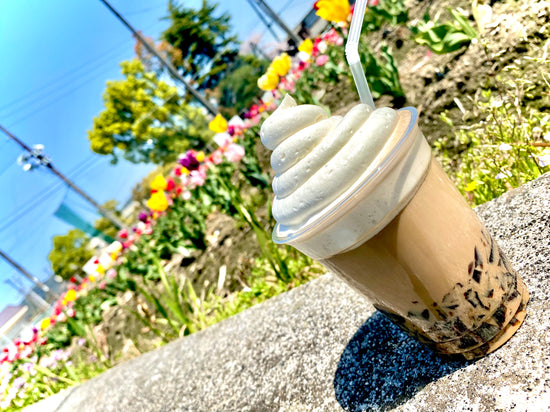 クラッシュコーヒーの生クリームトッピングドリンクの商品写真。飯岡小学校のチューリップ畑と青空をバックに撮影した画像