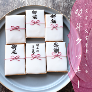 一つ一つ手書きする熨斗袋(蝶結び)のアイシングクッキーが6枚写った写真。その上に、ピンクの背景。白文字で『一文字一文字手書きする熨斗クッキー』の文字。